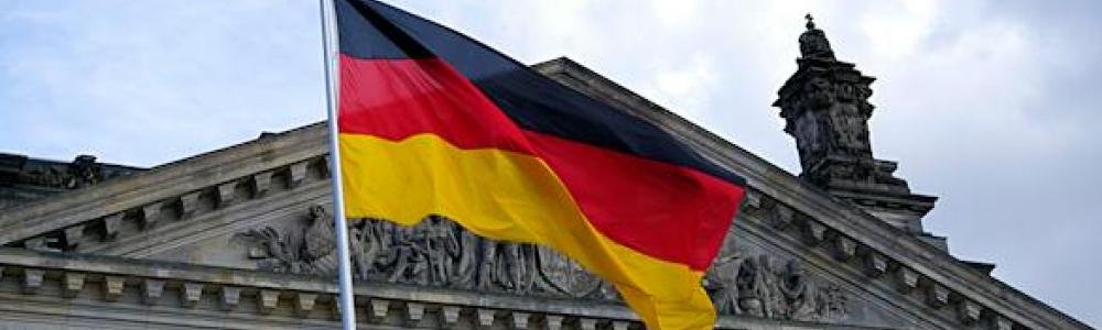 Fahne von Deutschland (Farben Schwarz-Rot-Gold) weht vor dem Reichstagsgebäude mit der Aufschrift Dem deutschen Volke. Zudem ist ein leicht bewölkter Himmel zu sehen.