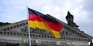 Fahne von Deutschland (Farben Schwarz-Rot-Gold) weht vor dem Reichstagsgebäude mit der Aufschrift Dem deutschen Volke. Zudem ist ein leicht bewölkter Himmel zu sehen.