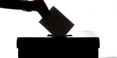 Hand steckt einen Brief in eine Wahlurne.