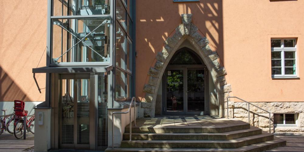 Eingang eines orangefarbenen Gebäudes mit Treppe und Fahrstuhl