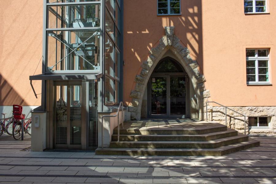Eingang eines orangefarbenen Gebäudes mit Treppe und Fahrstuhl