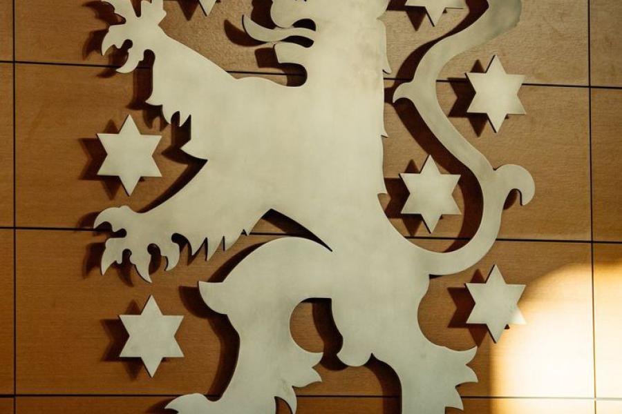 Ein stilisierter Löwe mit Krone und heraushängender Zunge an einer Holzwand, um ihn herum 8 Sterne