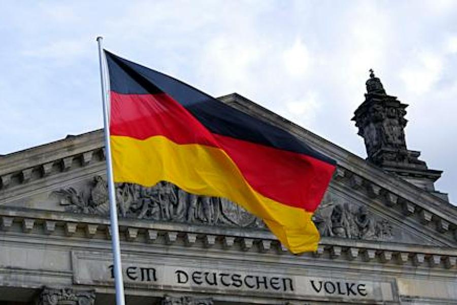 Fahne von Deutschland (Farben Schwarz-Rot-Gold) weht vor dem Reichstagsgebäude mit der Aufschrift Dem deutschen Volke. Zudem ist ein leicht bewölkter Himmel zu sehen.