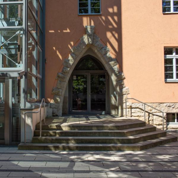 Eingang eines orangefarbenen Gebäudes mit Treppe und Fahrstuhl